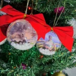 Lembrança de Natal personalizada em formato de bola com foto, decorada com laço vermelho e detalhes delicados, ideal para presentear e decorar a árvore de Natal.