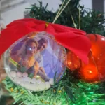 Enfeite de Natal personalizado em formato de bola com foto, acabamento artesanal, laço vermelho e detalhes decorativos, produzido pela Tekart Personalizados.