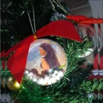 Bola de Natal personalizada com foto, decorada com laço vermelho e bolinhas de isopor, criando um enfeite natalino exclusivo produzido pela Tekart Personalizados.